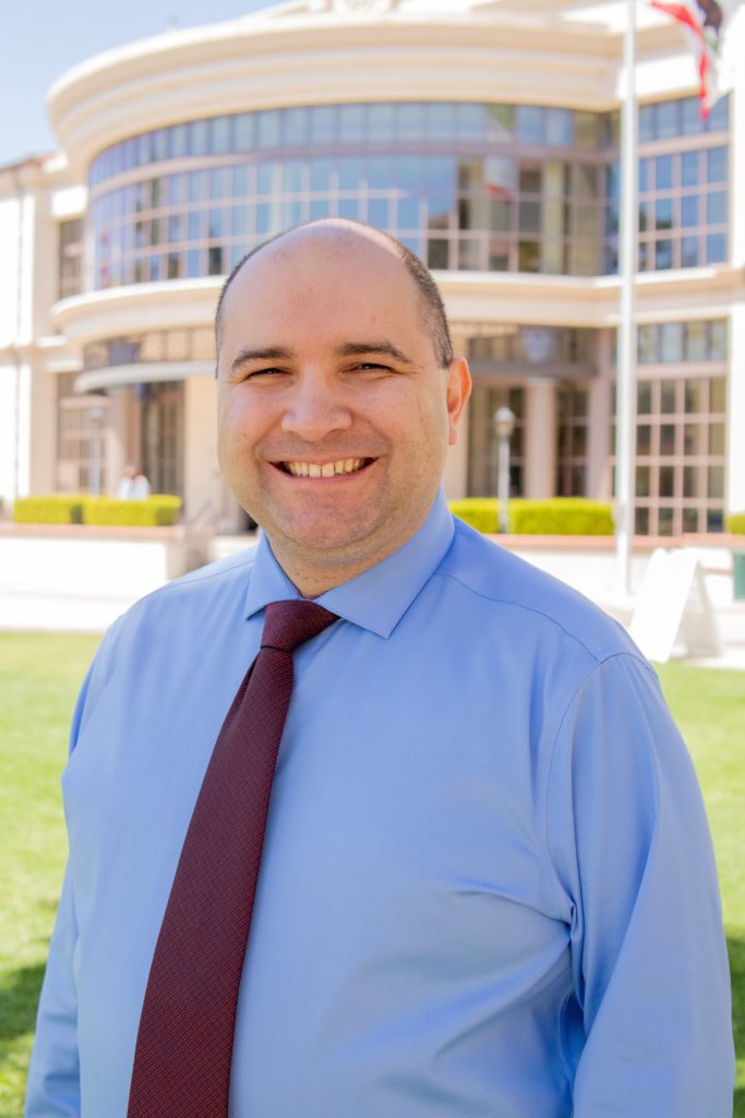 Person in blue shirt and red tie standing in front of Fullerton College library